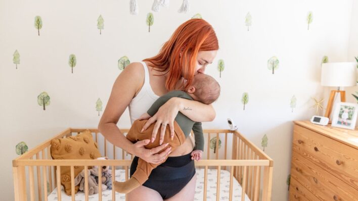 Un primer plano de un bebé recién nacido durmiendo profundamente sobre una manta blanca suave. El bebé lleva un pelele blanco con detalles de rayas azules en los puños y el pecho, junto con un gorro a juego. La imagen transmite una sensación de calma, suavidad y comodidad.