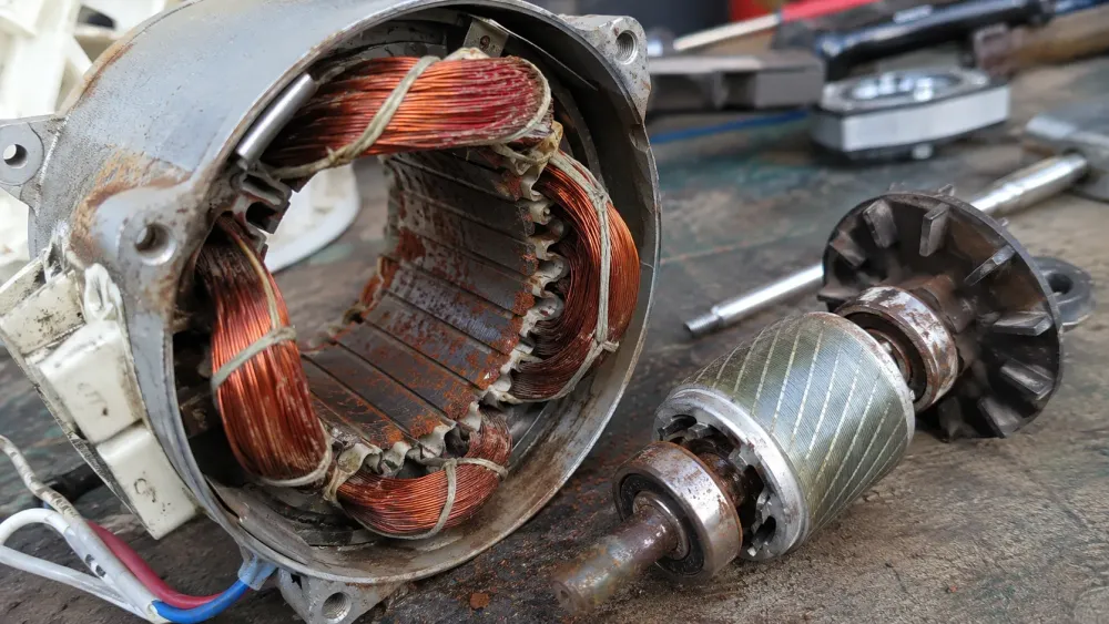 Motor de ventilador eléctrico desmontado sobre una mesa de trabajo, con el estator abierto, bobinas de cobre visibles, óxido en el núcleo metálico y el rotor separado al lado. La imagen muestra corrosión, polvo de óxido y desgaste interno del motor, relacionada con fallos, ruido, calentamiento y riesgo de cortocircuito.