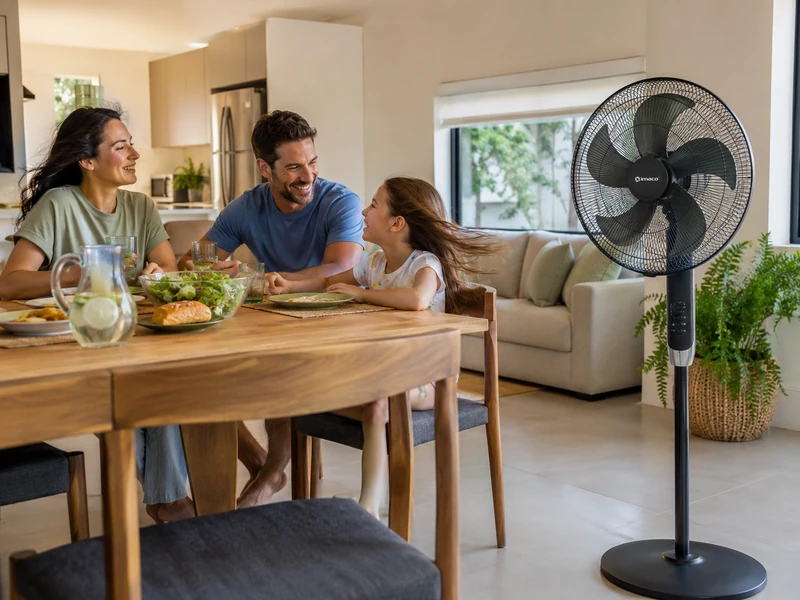 Familia sentada en un comedor luminoso con un ventilador doméstico de pie de cinco aspas colocado cerca para proporcionar una brisa cómoda durante la vida diaria en casa.